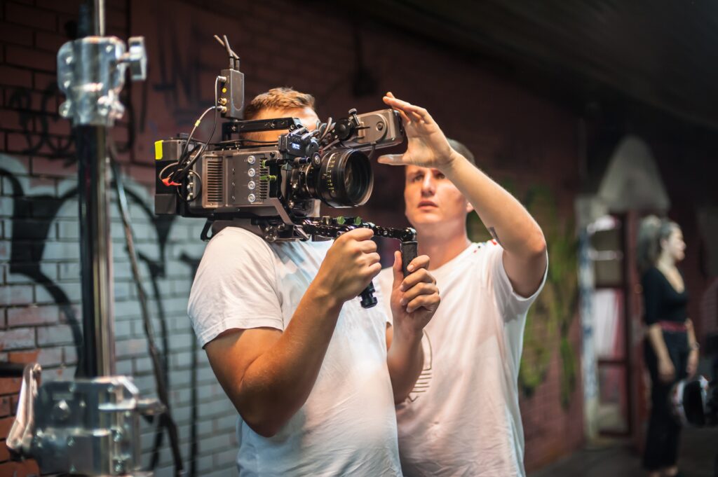 Crew members adjust a professional camera rig in an urban setting, preparing for a film shoot amid graffiti-covered walls.