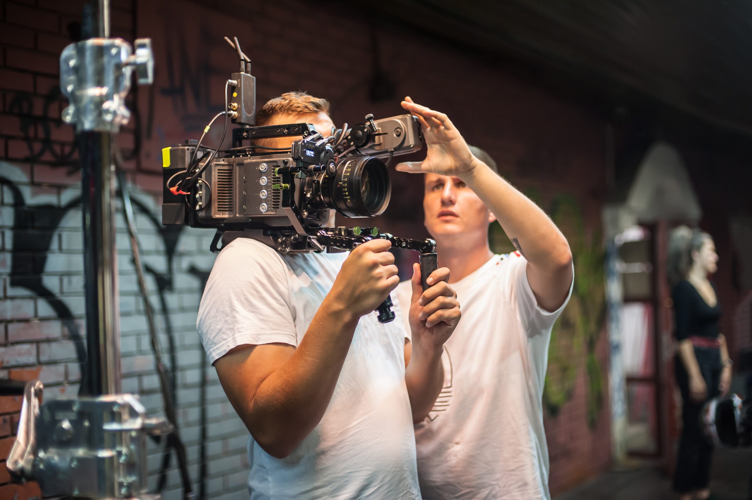 Crew members adjust a professional camera rig in an urban setting, preparing for a film shoot amid graffiti-covered walls.